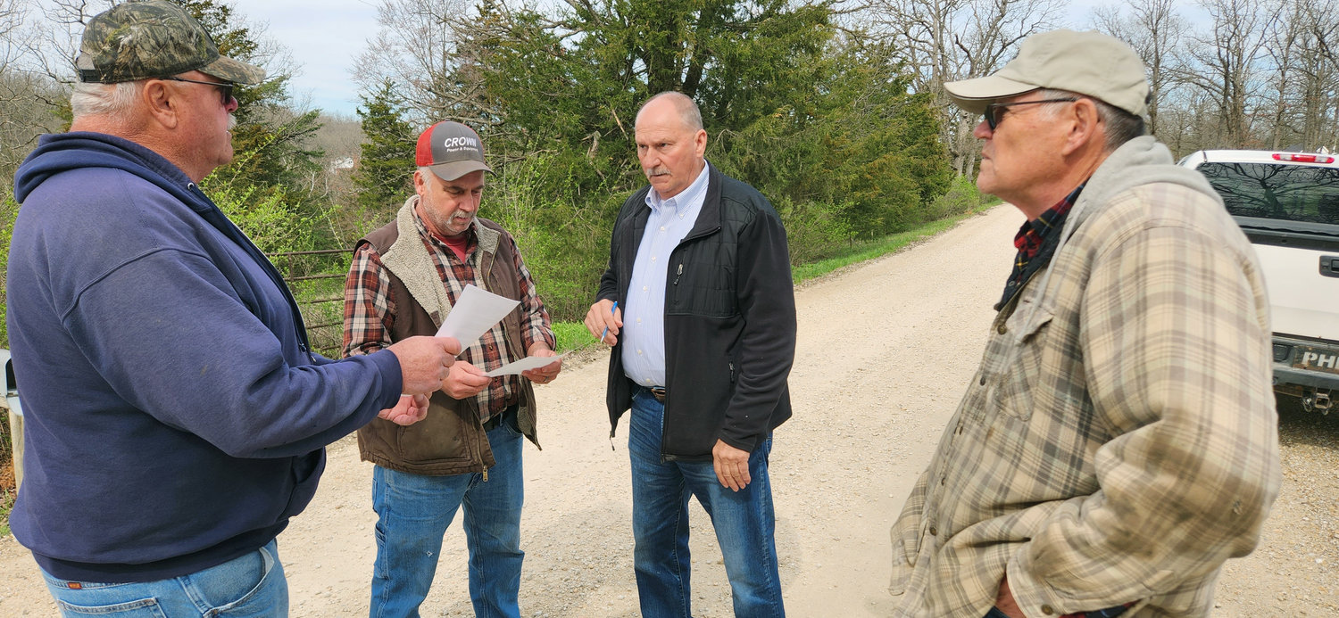 Old Woollam Road landowners Dwayne Drewell (left) and Jeff Limberg on Thursday morning read over easement agreements with Southern District Commissioner Jerry Lairmore (middle) after their meeting earlier at Owensville City Hall with members of the county governing body. Gene Menz, a neighbor to the south, was also participating in the roadside discussion.  Drewell and Limberg each granted an easement onto their frontage which will help residents of the road qualify for participation in a voluntary request for having a chip-and-seal hard surface installed. One more neighbor was being asked to participate to give commissioners a 1.5-mile stretch of road to consider for future planning.
